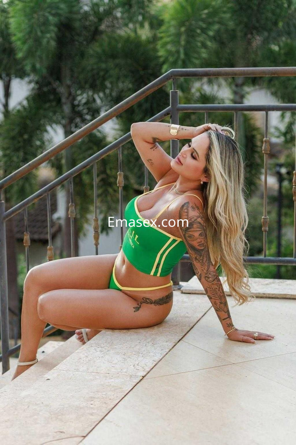 Puta con cabello rubio y largo, vistiendo bikini verde y amarillo, posando en una terraza en Tenerife.