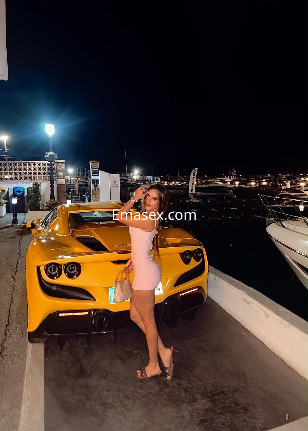 Puta en Vigo, luciendo un vestido rosa ajustado y sandalias, posando junto a un coche deportivo amarillo.