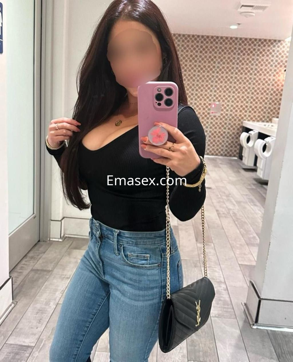 Escort en Cádiz con cabello largo y oscuro, vestida con blusa negra ajustada y jeans, posando frente a un espejo.