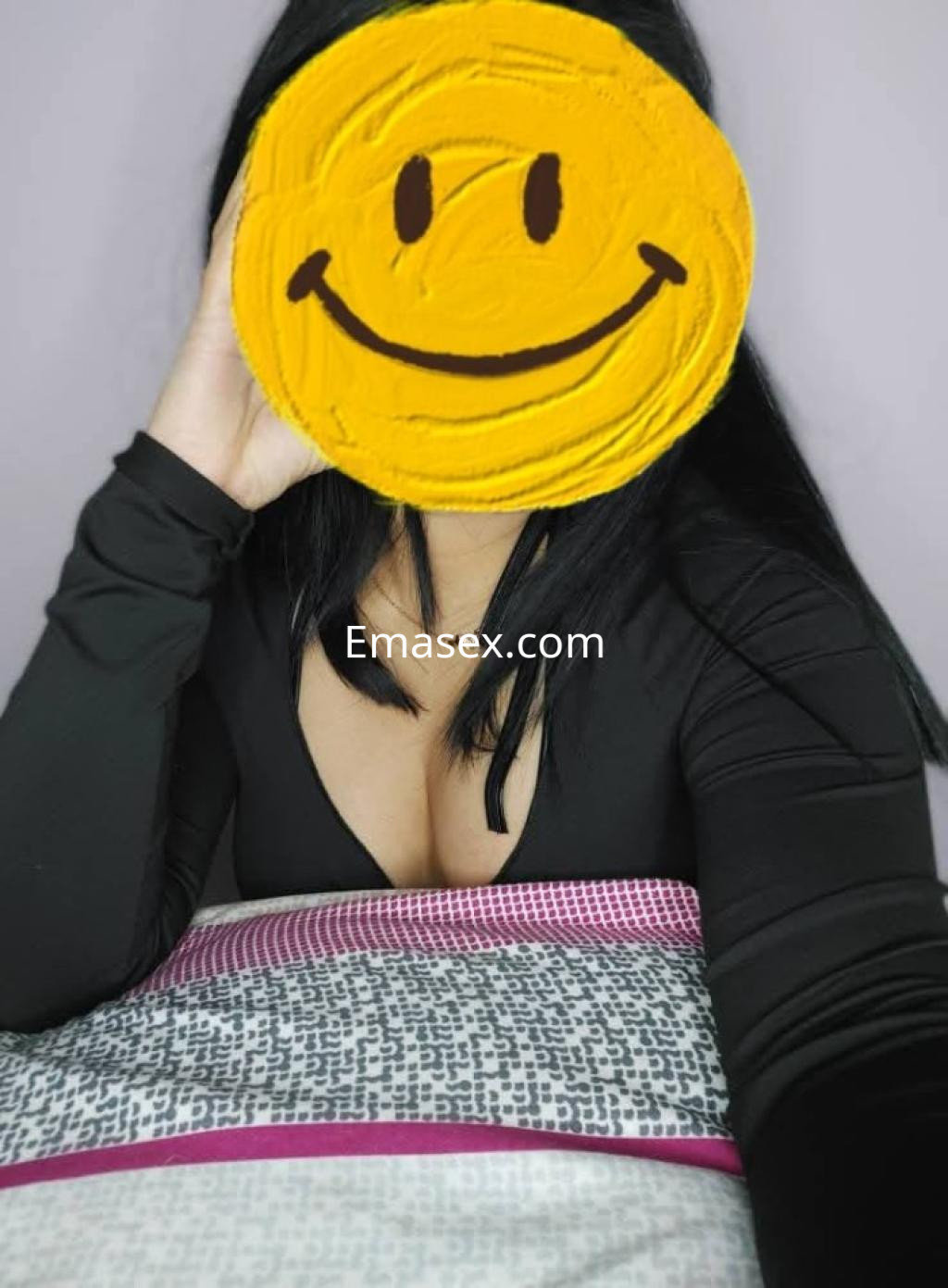 Escort en Burgos con cabello largo y oscuro, vestida con una blusa negra y posando sobre la cama.