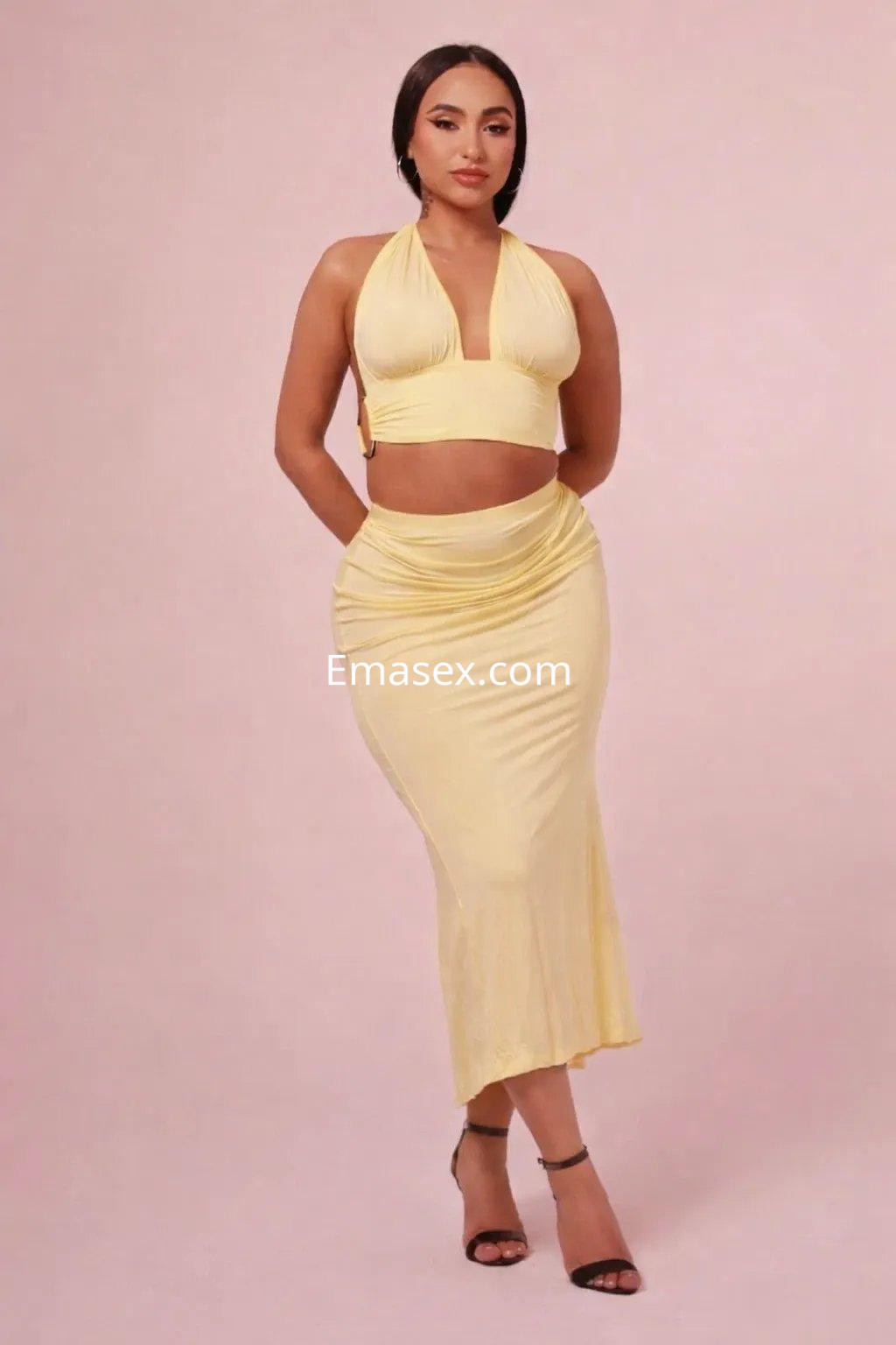 Escort en Gijón luciendo un conjunto amarillo que resalta su figura, con un fondo neutro y elegante.