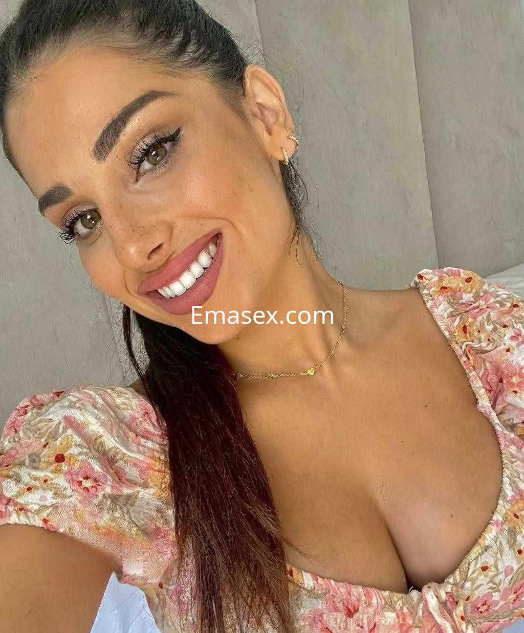 Puta en Valencia sonríe a la cámara, luciendo un vestido floral con escote y un peinado recogido.