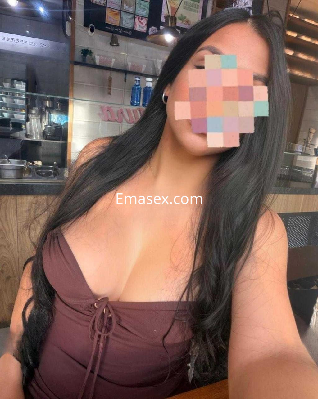 Escort en Madrid con una blusa marrón de escote pronunciado, posando en un entorno de cafetería.