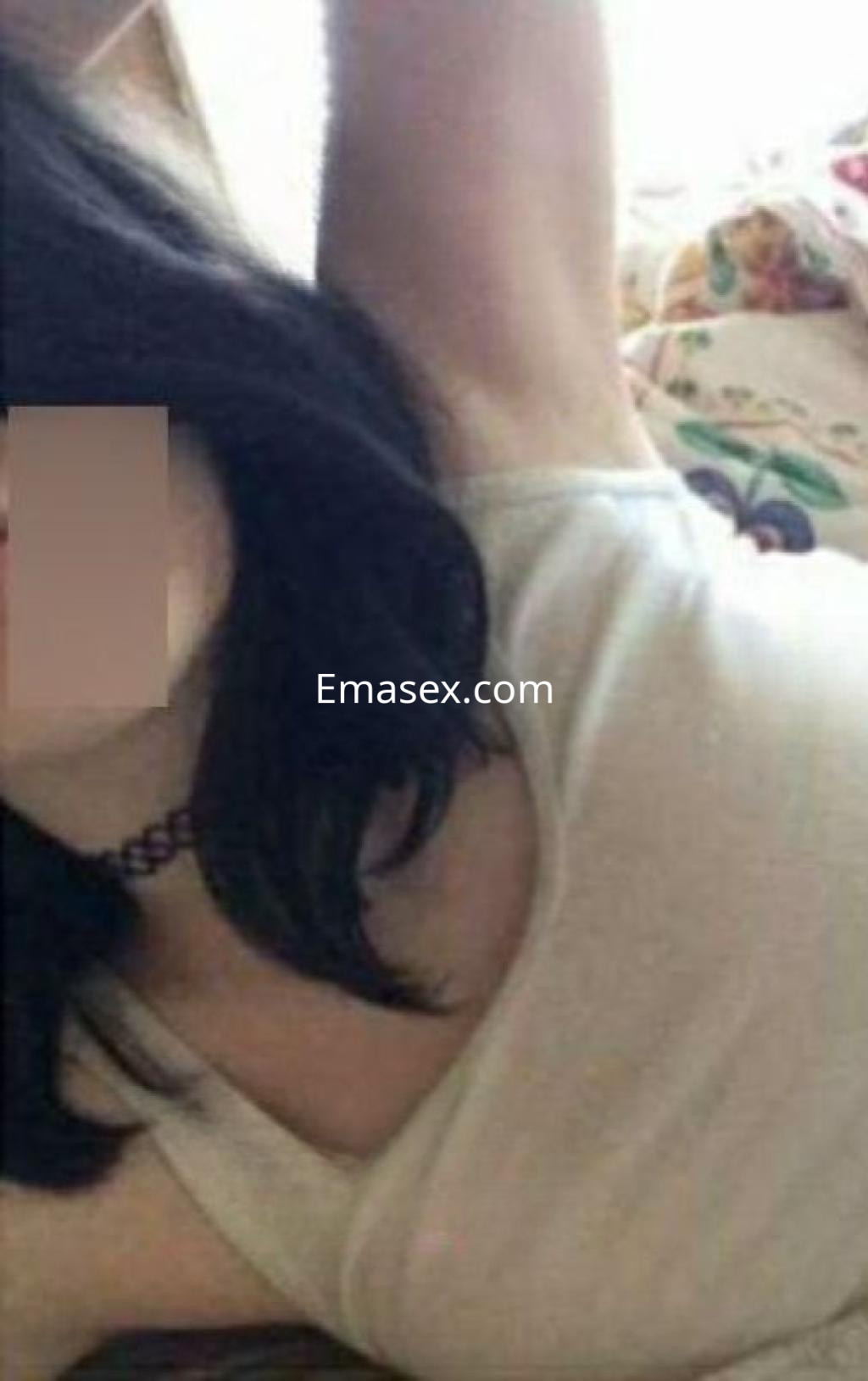 Puta en Madrid con cabello oscuro, lleva una blusa sin mangas clara y se encuentra recostada en la cama.