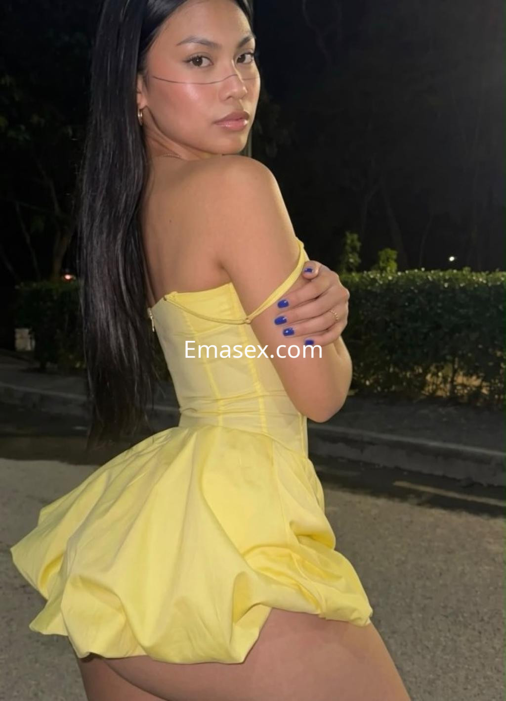 Escort en Santander luciendo un vestido amarillo ajustado y corto, posando de espaldas en un ambiente nocturno.