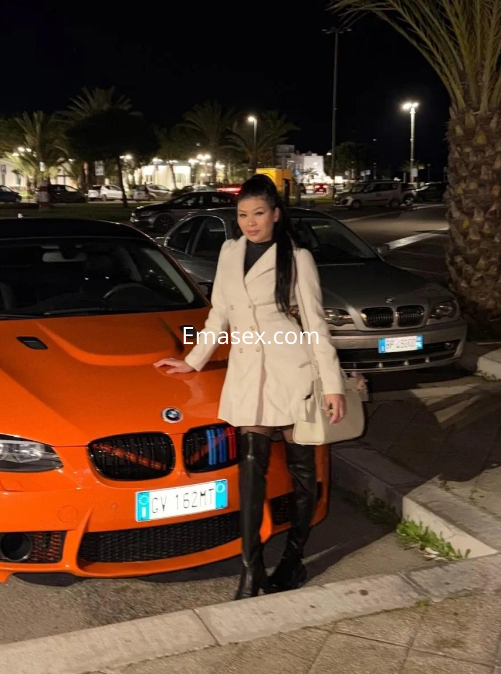 La puta viste un abrigo blanco y botas altas de cuero, posando junto a un coche deportivo naranja en Vigo.