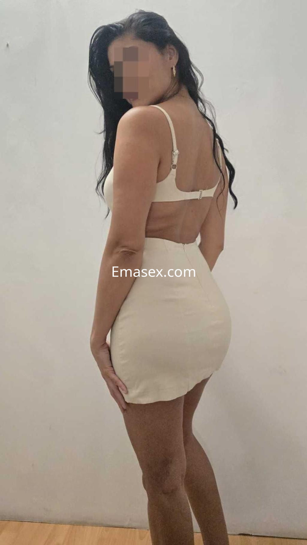 Puta en Barcelona con cabello largo y rizado, vistiendo un vestido ajustado blanco, posando de espaldas.