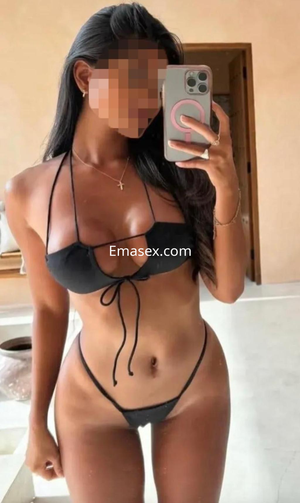 Escort en Vitoria luciendo un bikini negro mientras se toma una selfie en un entorno interior moderno.