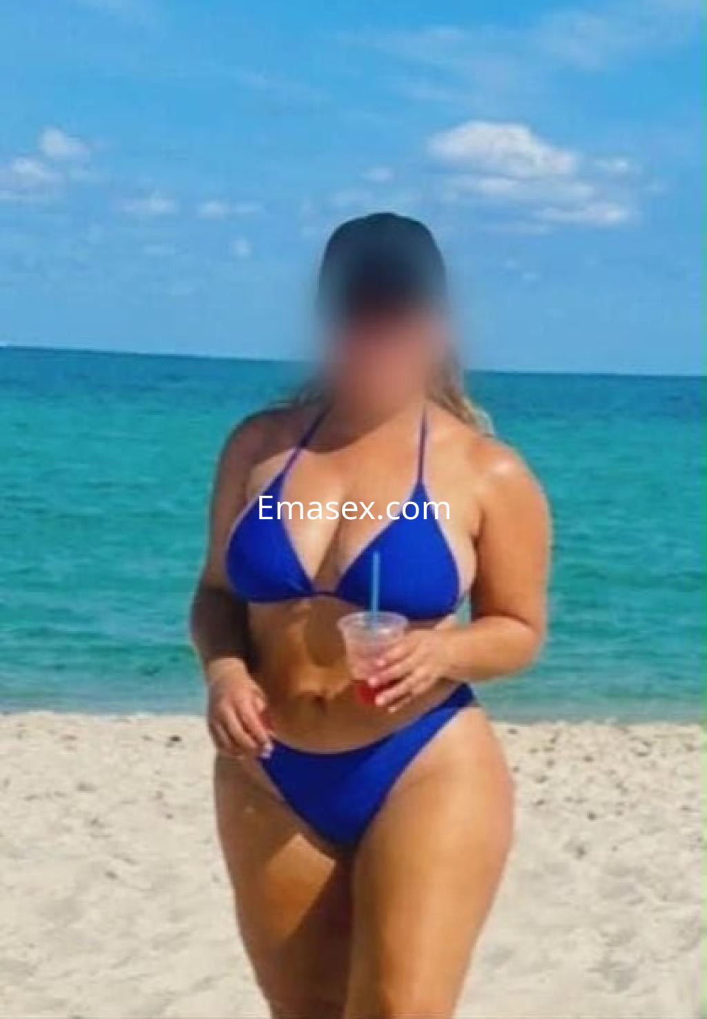 Puta en la playa de Vitoria, luciendo un bikini azul y sosteniendo una bebida, con cabello largo y lacio.