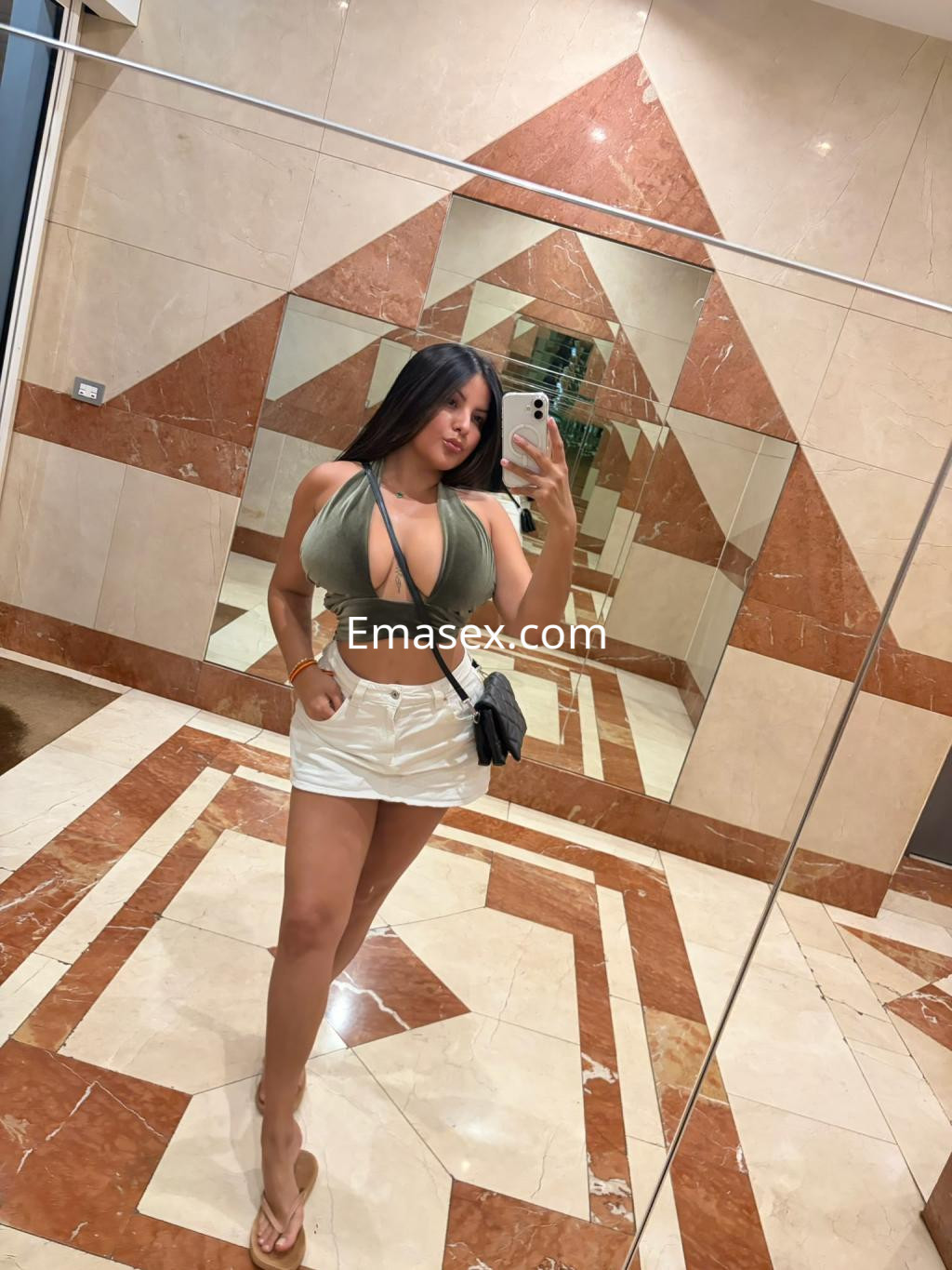 Escort en Donosti tomando una selfie en el espejo, vistiendo un top verde y una falda corta blanca.