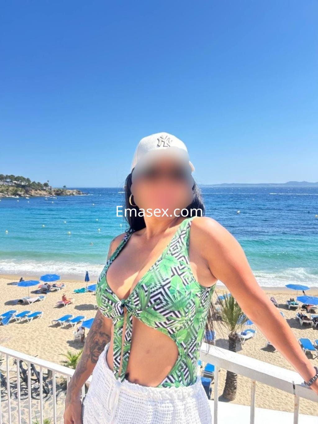 Escort en Castellón luciendo un traje de baño verde y un gorro blanco, con playa y mar de fondo.