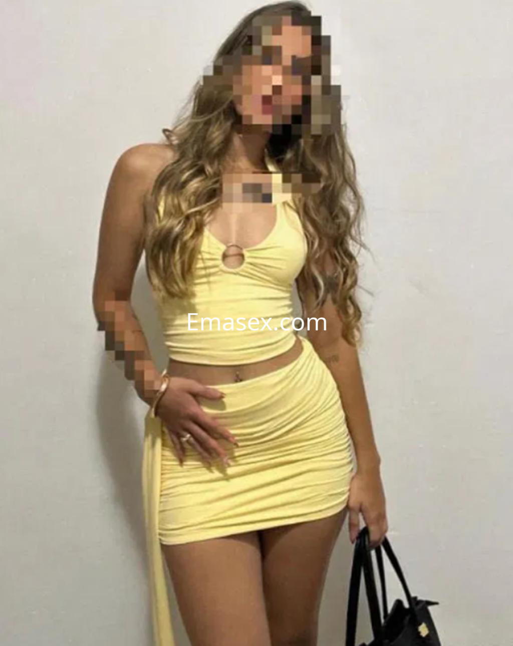 La escort luce un conjunto amarillo de dos piezas, posando con una bolsa negra en un entorno interior en Bilbao.