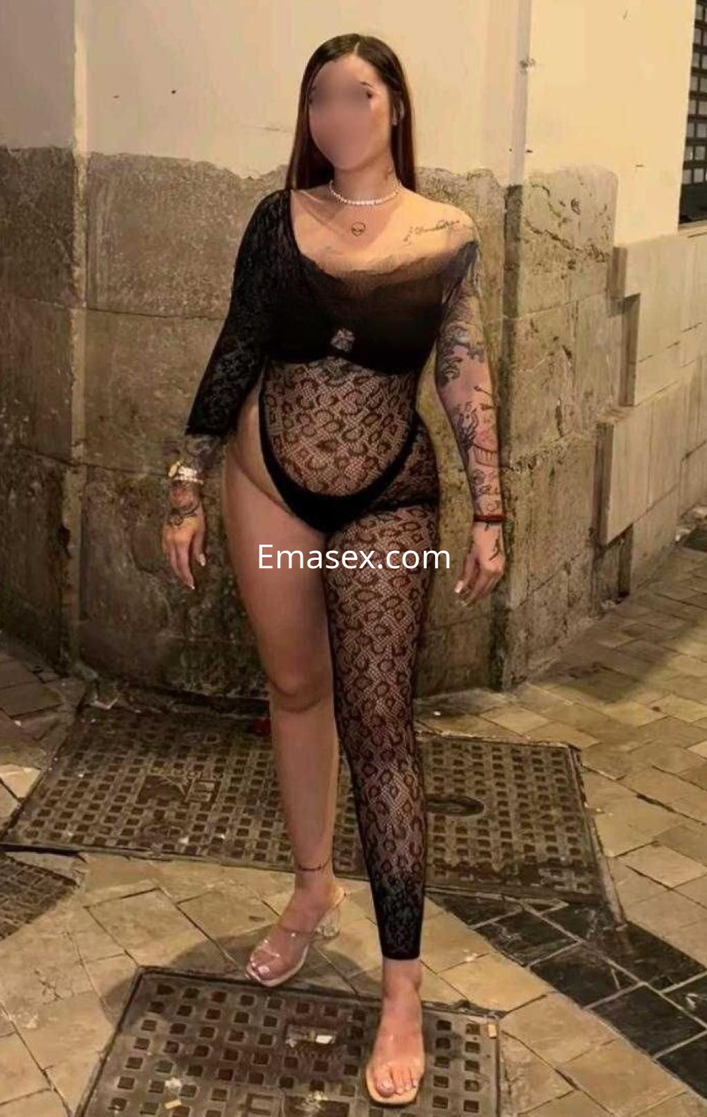 Puta de cabello largo y lacio, viste un body negro con detalles de encaje, en una calle de Barcelona.