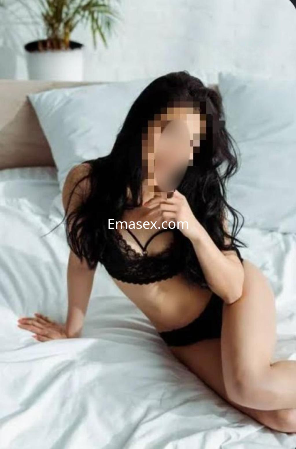 Escort en Pontevedra sentada en una cama, luciendo lencería negra y con cabello largo y oscuro.