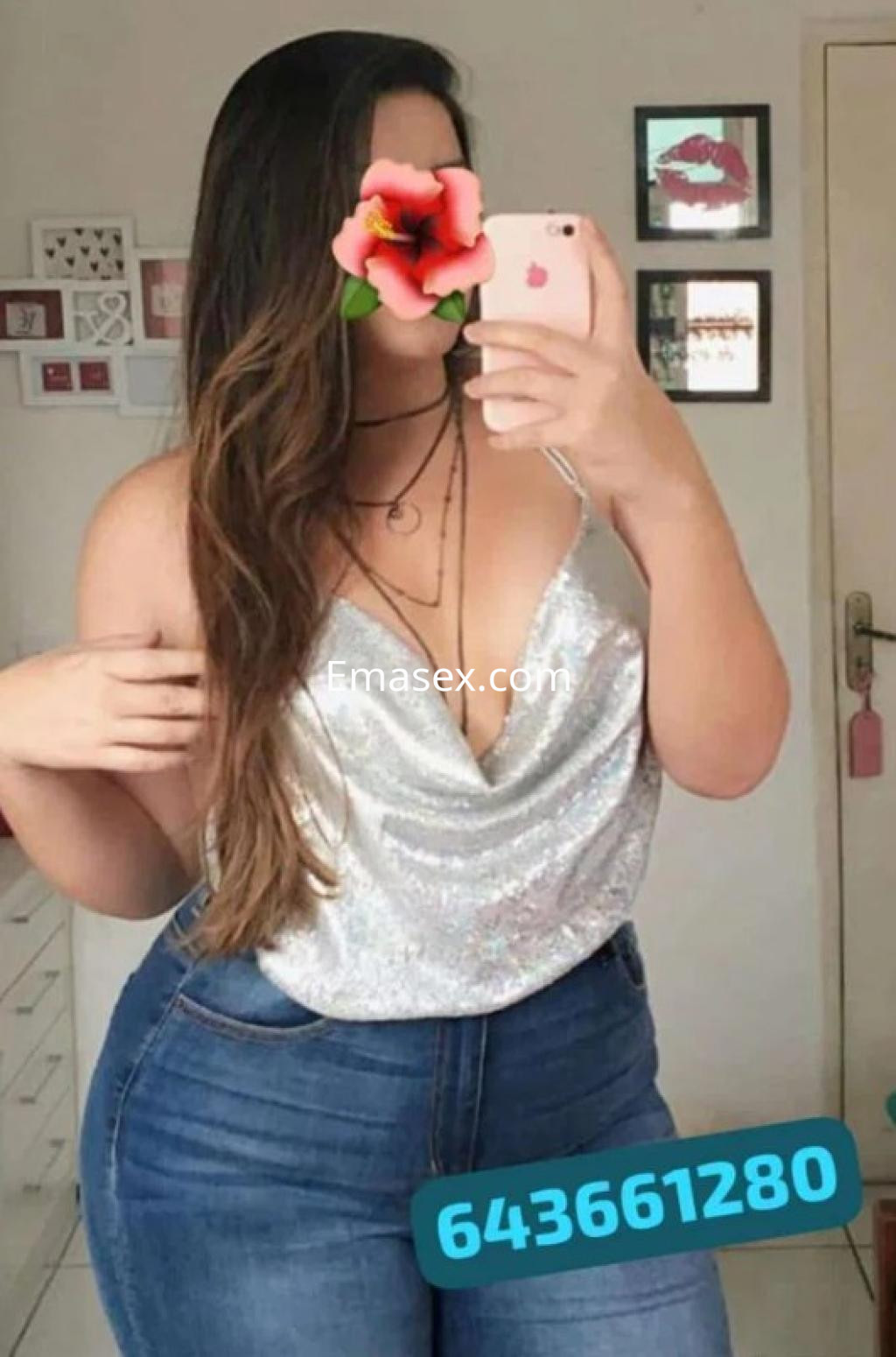 Escort en Burgos con blusa brillante y jeans ajustados, posando frente a un espejo con cabello largo.