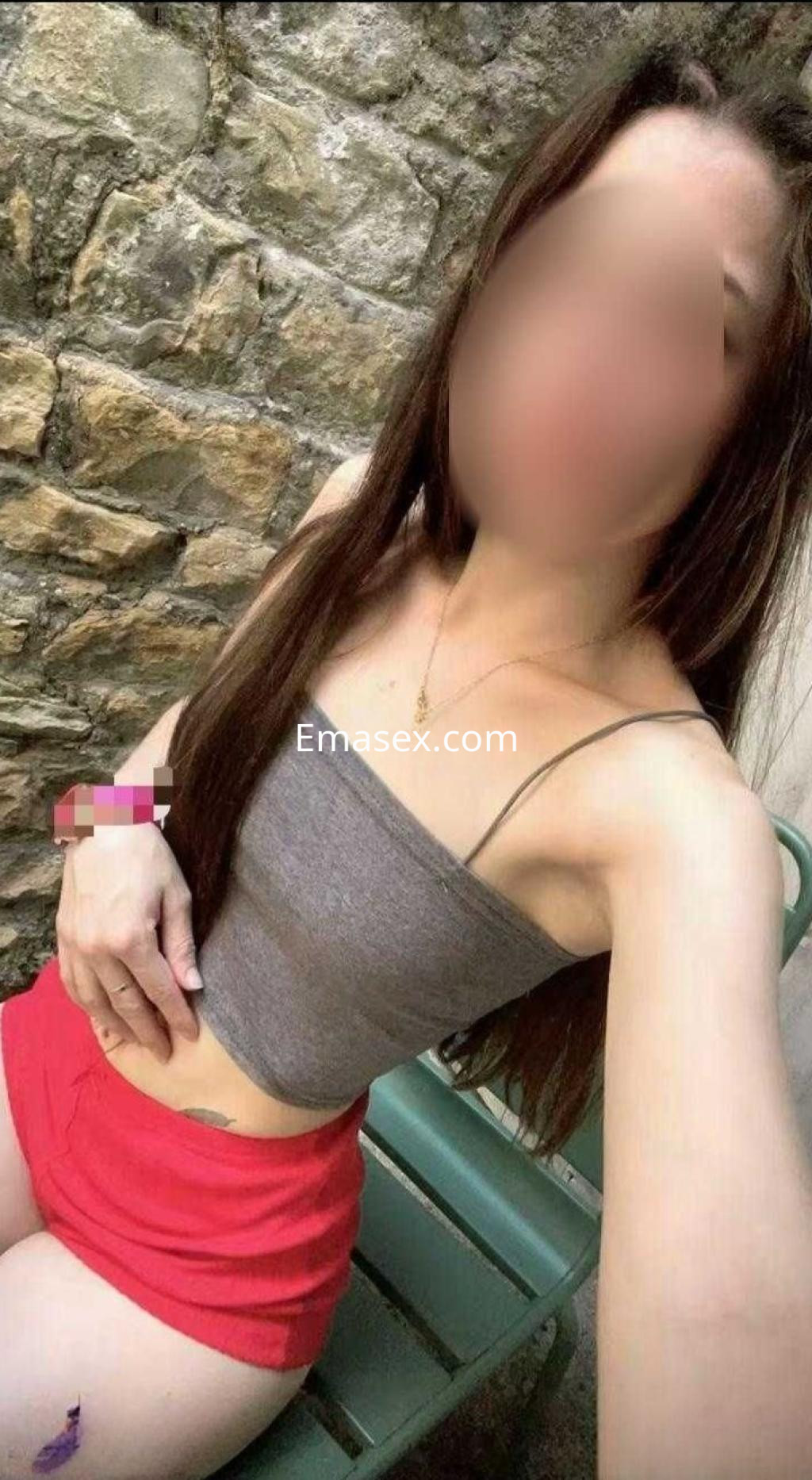 Puta de cabello largo y lacio, viste un top gris y una falda corta roja en un entorno exterior en Madrid.