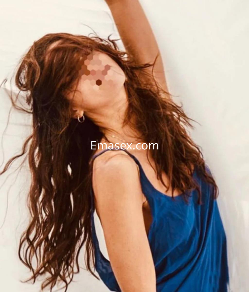 Puta con cabello largo y rizado, vistiendo una blusa azul, posando en un fondo claro en Pamplona.