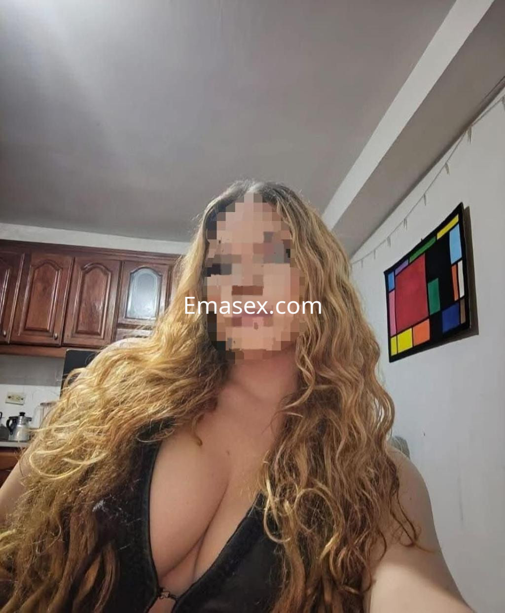 Escort en Málaga con cabello rizado y largo, usando un top oscuro en un ambiente interior con cocina.