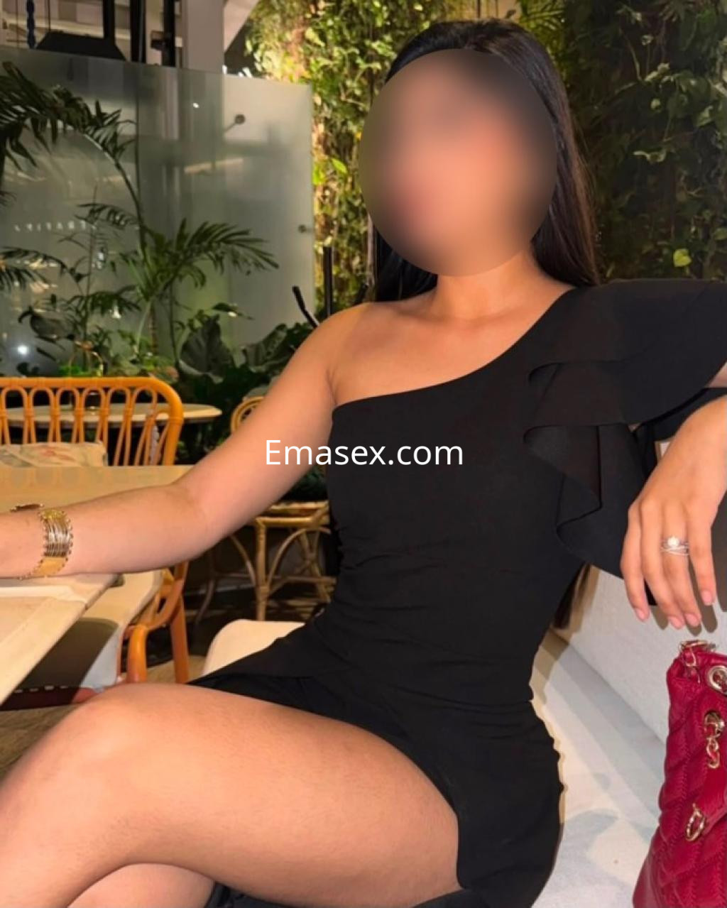 Puta en Tarragona viste un vestido negro de un solo hombro, posando con una pierna cruzada en un ambiente elegante.
