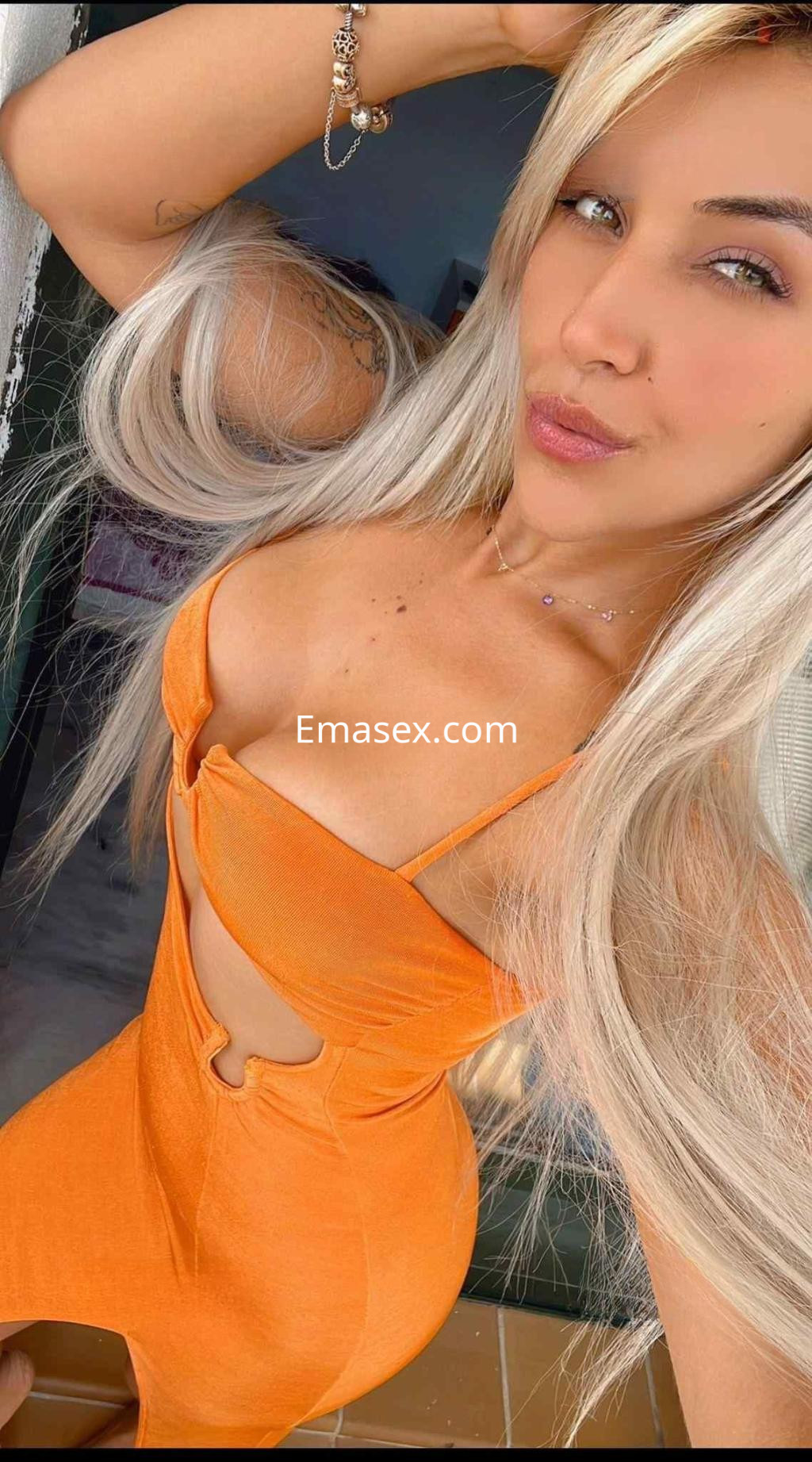 La puta luce un vestido naranja ajustado que resalta su figura, con cabello largo y lacio en Málaga.
