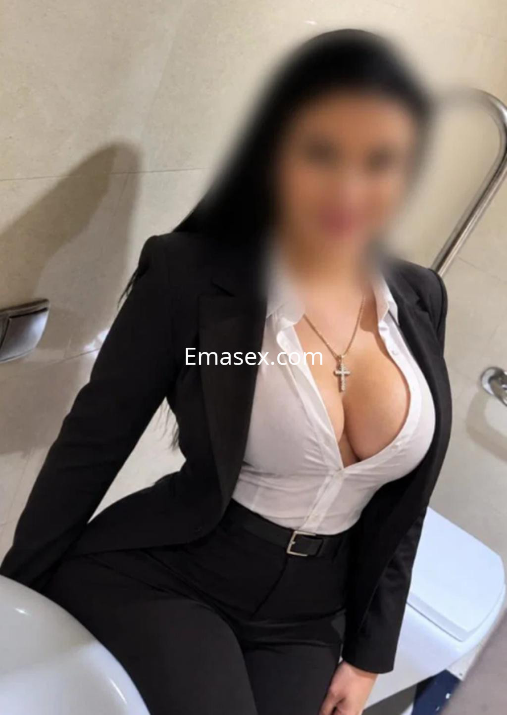 Puta en Santander viste un traje negro ajustado, con blusa blanca que resalta su escote mientras posa en un baño.