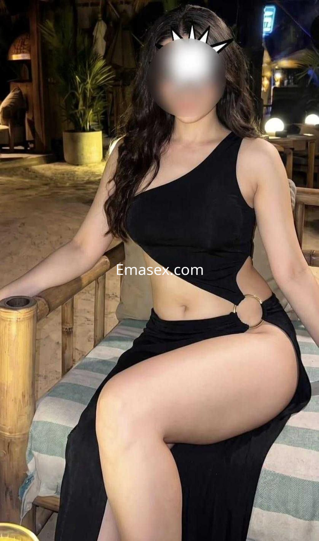 Escort en Madrid sentada en una silla, vistiendo un vestido negro asimétrico que realza su figura.