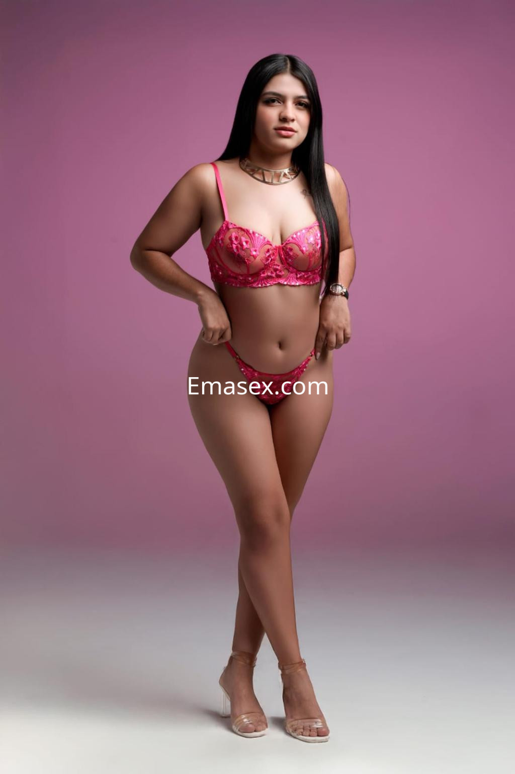 Escort en Vigo con cabello largo y lacio, vistiendo un conjunto de lencería rosa y tacones transparentes.