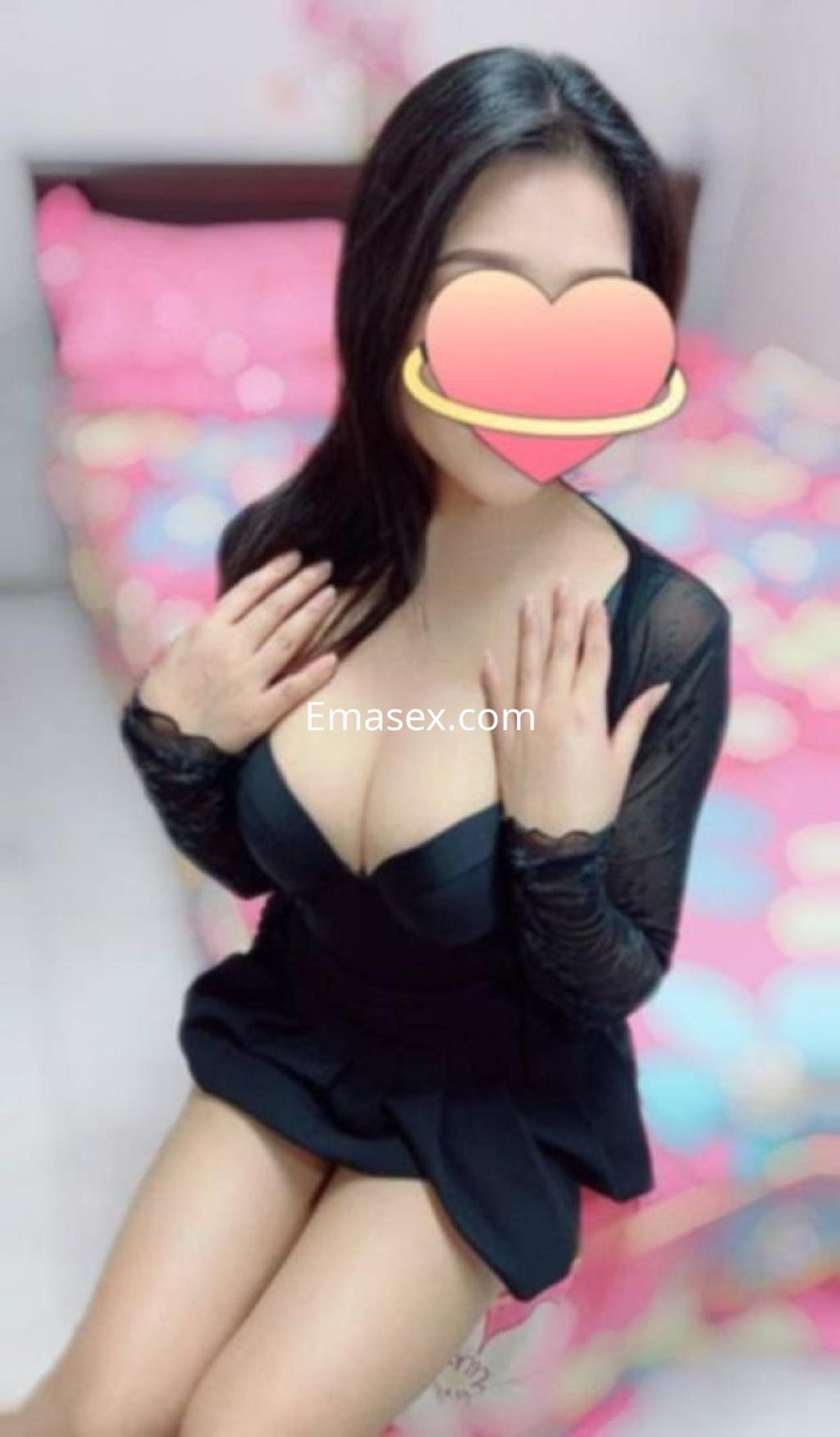 Puta en Madrid, con vestido oscuro de escote pronunciado, sentada en una cama con sábanas coloridas.