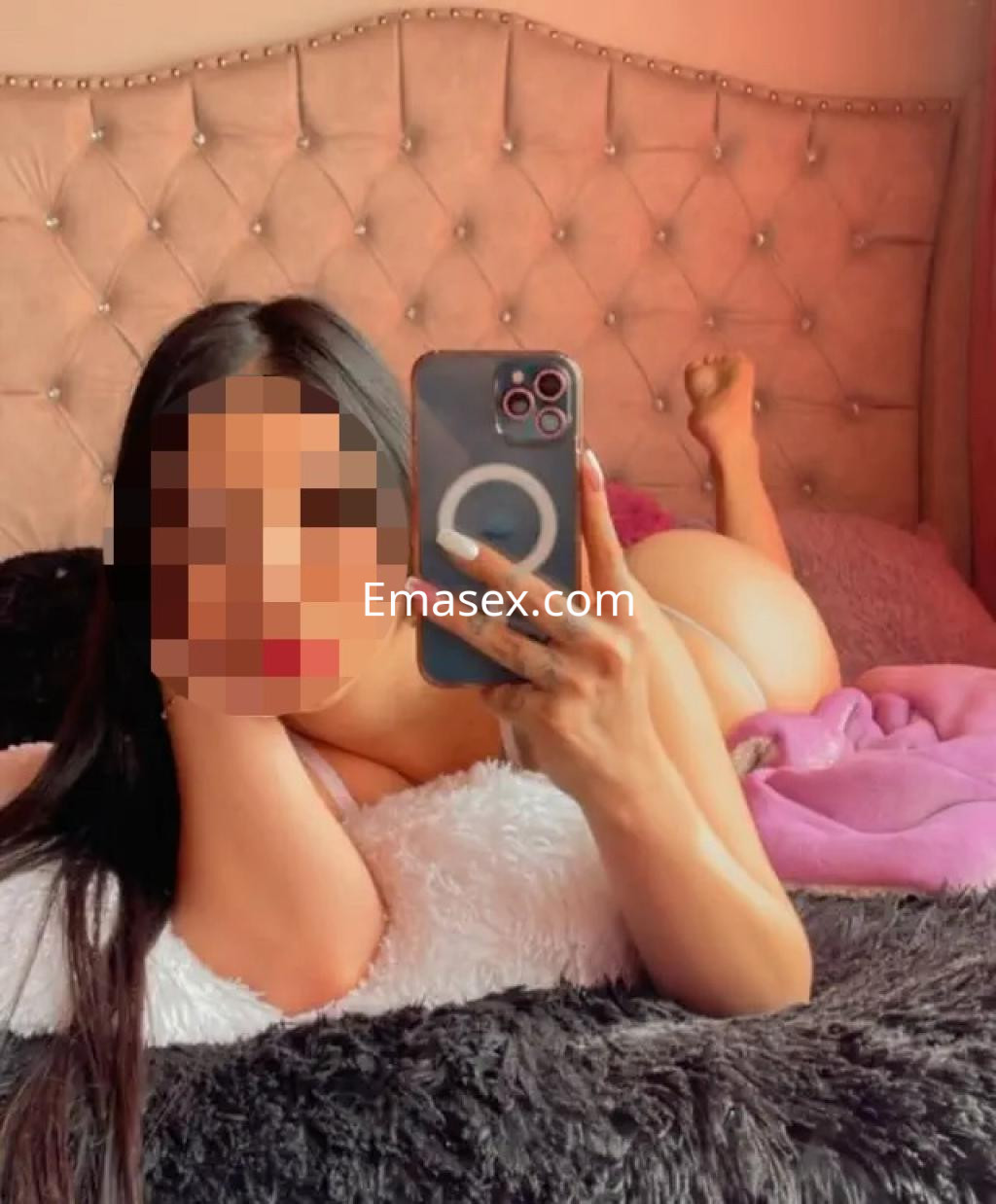 Escort reclinada sobre una cama con sábanas suaves, mostrando su cabello largo y posando con el teléfono en Lleida.
