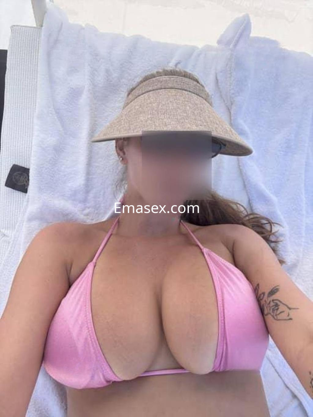 Puta en Lugo con un bikini rosa, descansando sobre una toalla blanca y usando un sombrero de ala ancha.