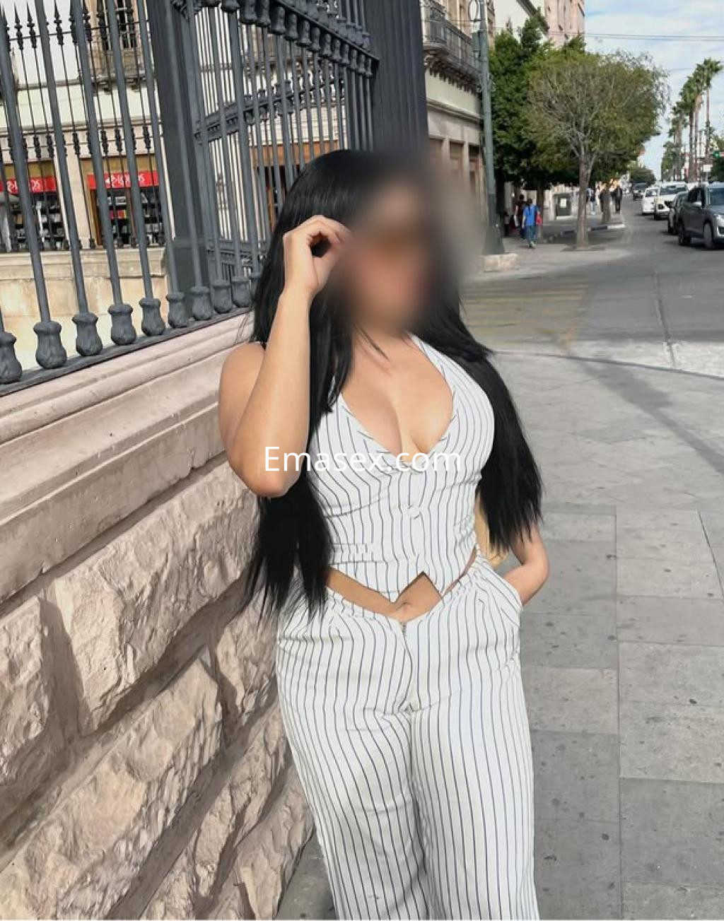 Escort en Santiago viste un conjunto de dos piezas a rayas, con cabello largo y lacio, posando de pie junto a una pared.