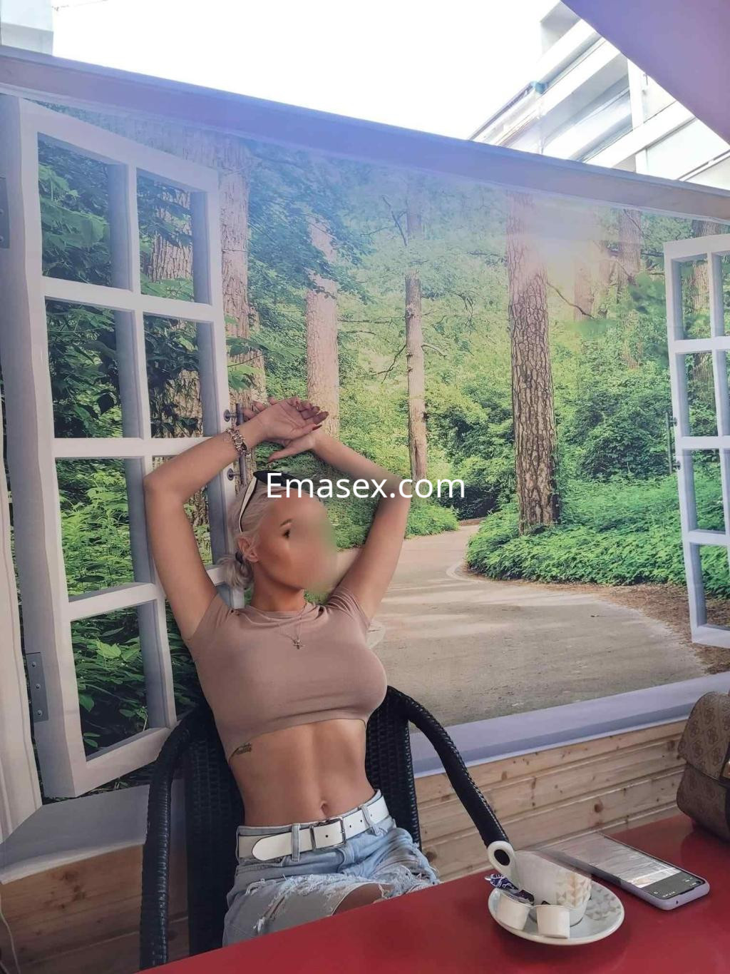 Escort en Toledo sentada en una silla, con top ajustado y pantalones cortos, en un ambiente natural.