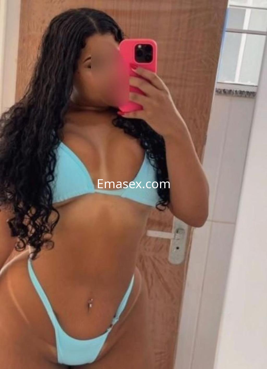 Puta de piel morena con cabello rizado y un bikini azul, posando en un espejo en Madrid.