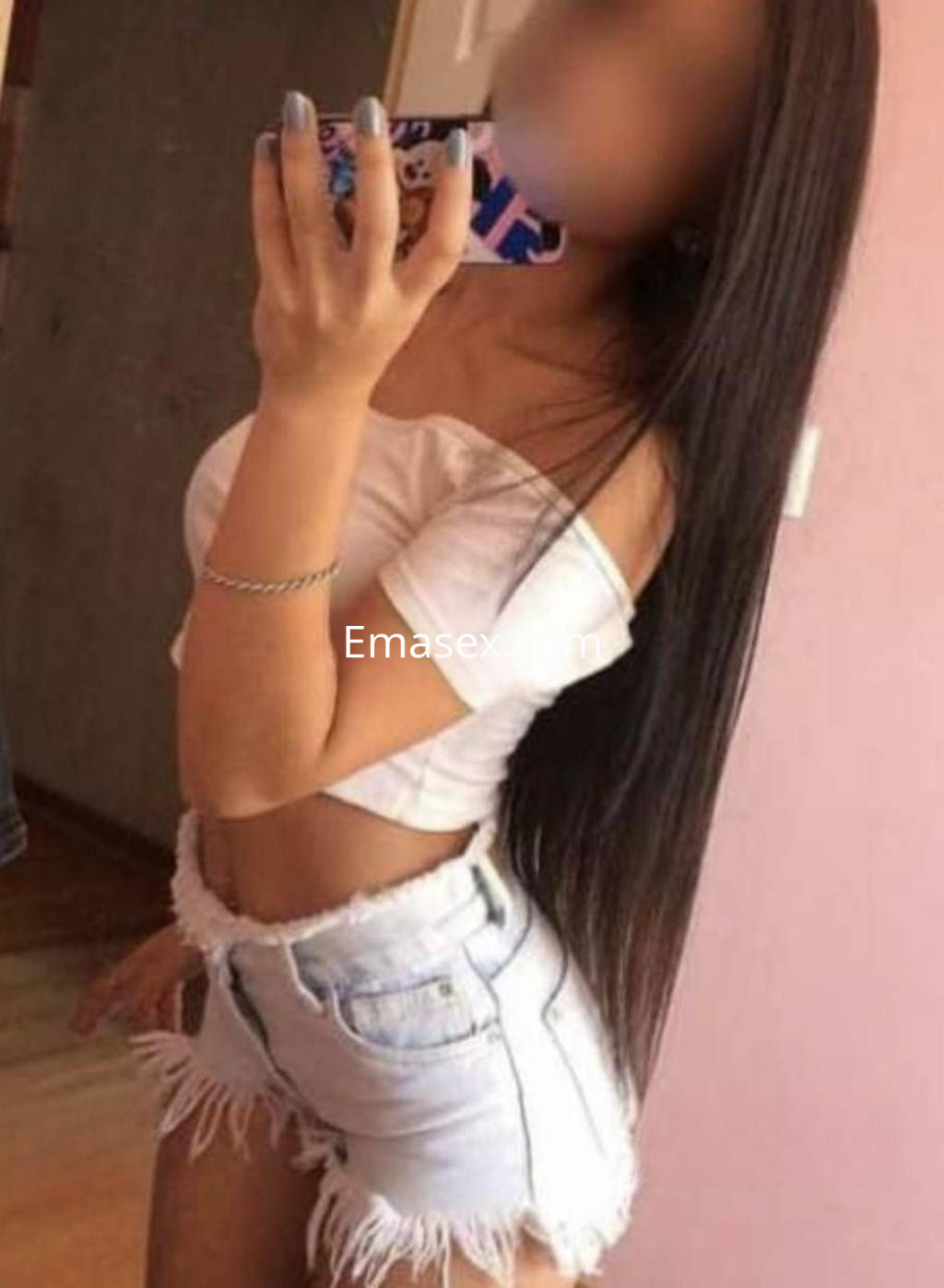Escort en Madrid se presenta con una blusa blanca off-shoulder y shorts de mezclilla, mostrando su largo cabello lacio.