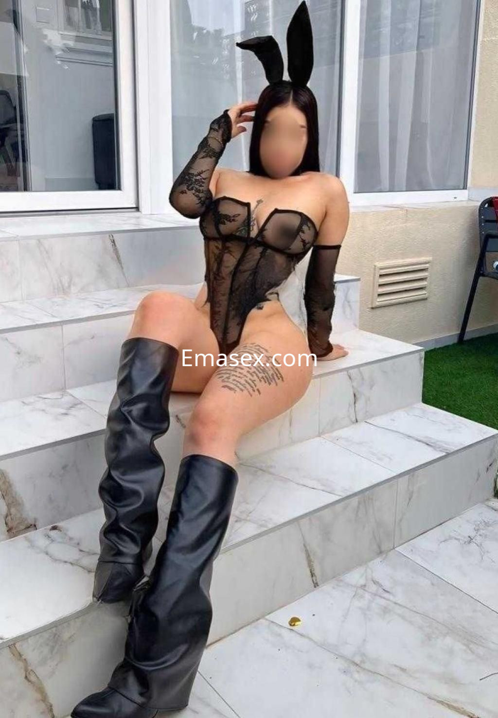 Escort en Alicante sentada en escaleras, vistiendo un bodysuit negro con detalles de encaje y botas altas.