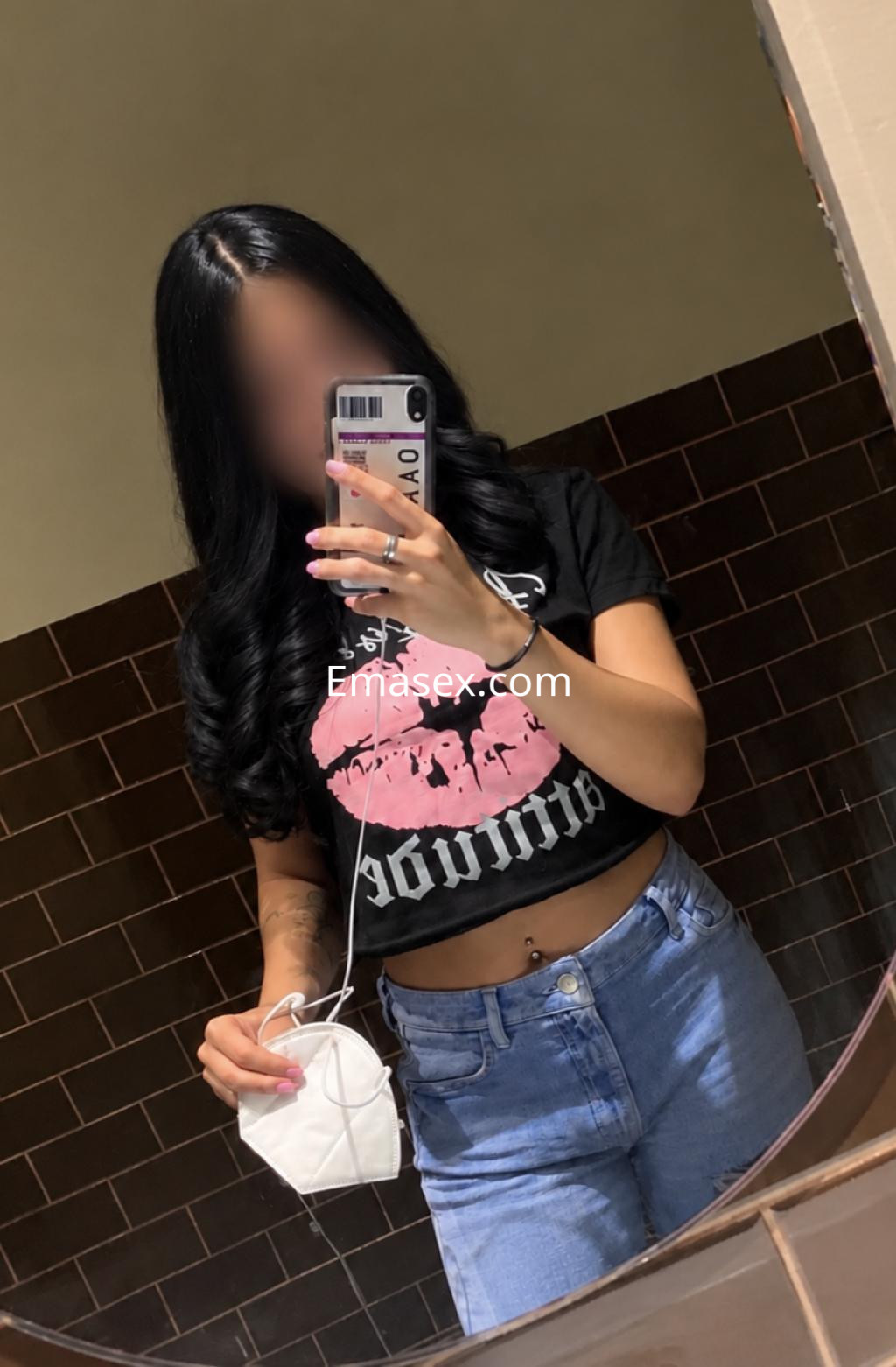 Puta en Santander tomando un autorretrato en el espejo, con camiseta negra y jeans, luciendo cabello largo y ondulado.