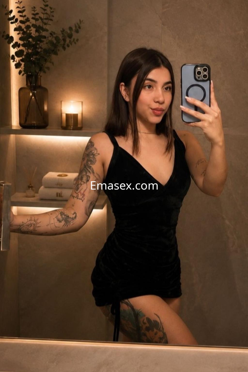 Puta en Bilbao se toma una selfie en un baño moderno, luciendo un vestido negro y mostrando sus tatuajes.