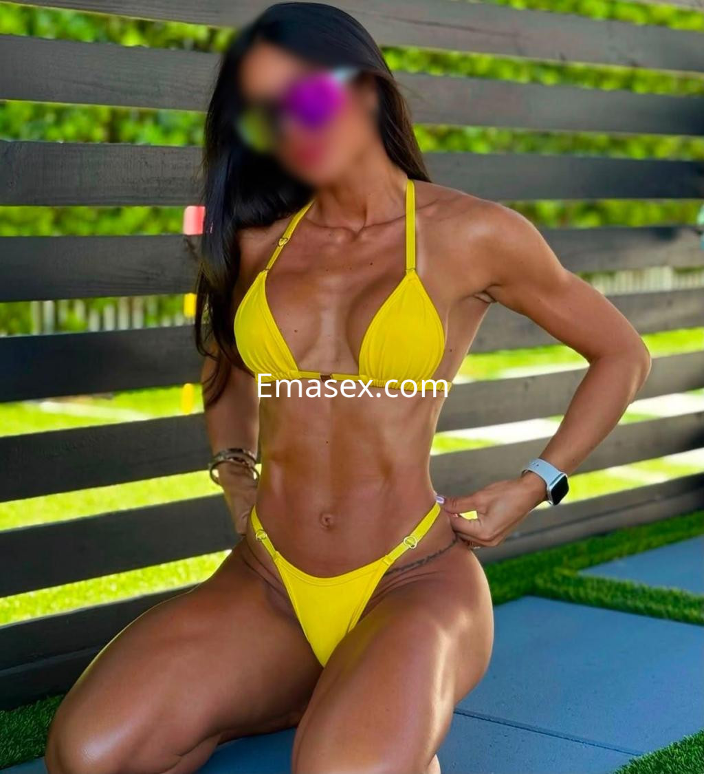 Puta en Donosti luciendo un bikini amarillo, posando de rodillas y mostrando su figura tonificada en un entorno verde.