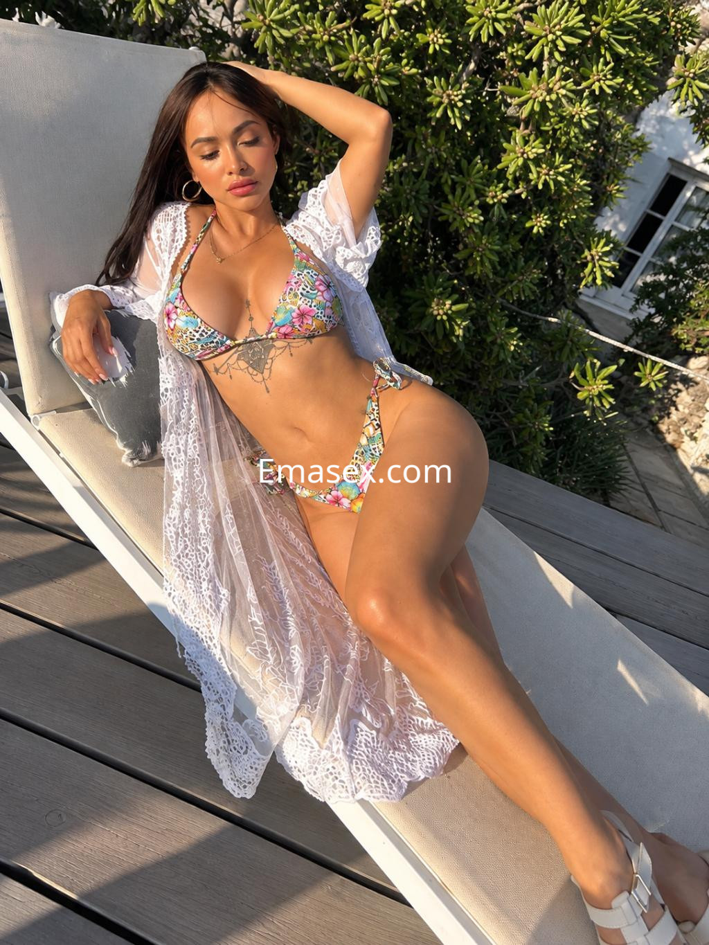 Escort en Santander muestra su figura en un bikini colorido con un kimono blanco, descansando en una tumbona.