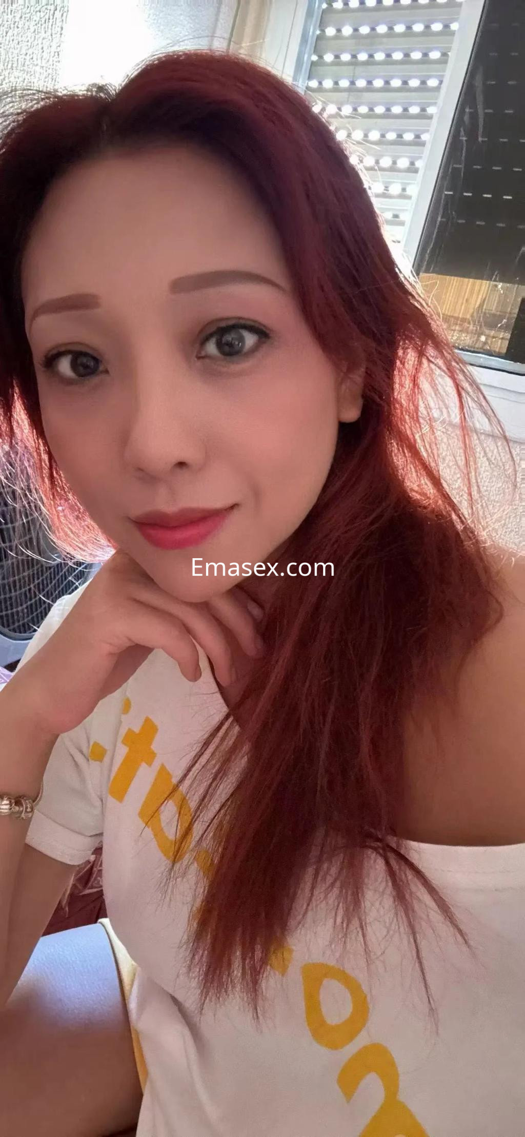 Puta con cabello largo y rojizo, usando una blusa blanca y posando de manera coqueta en Alicante.