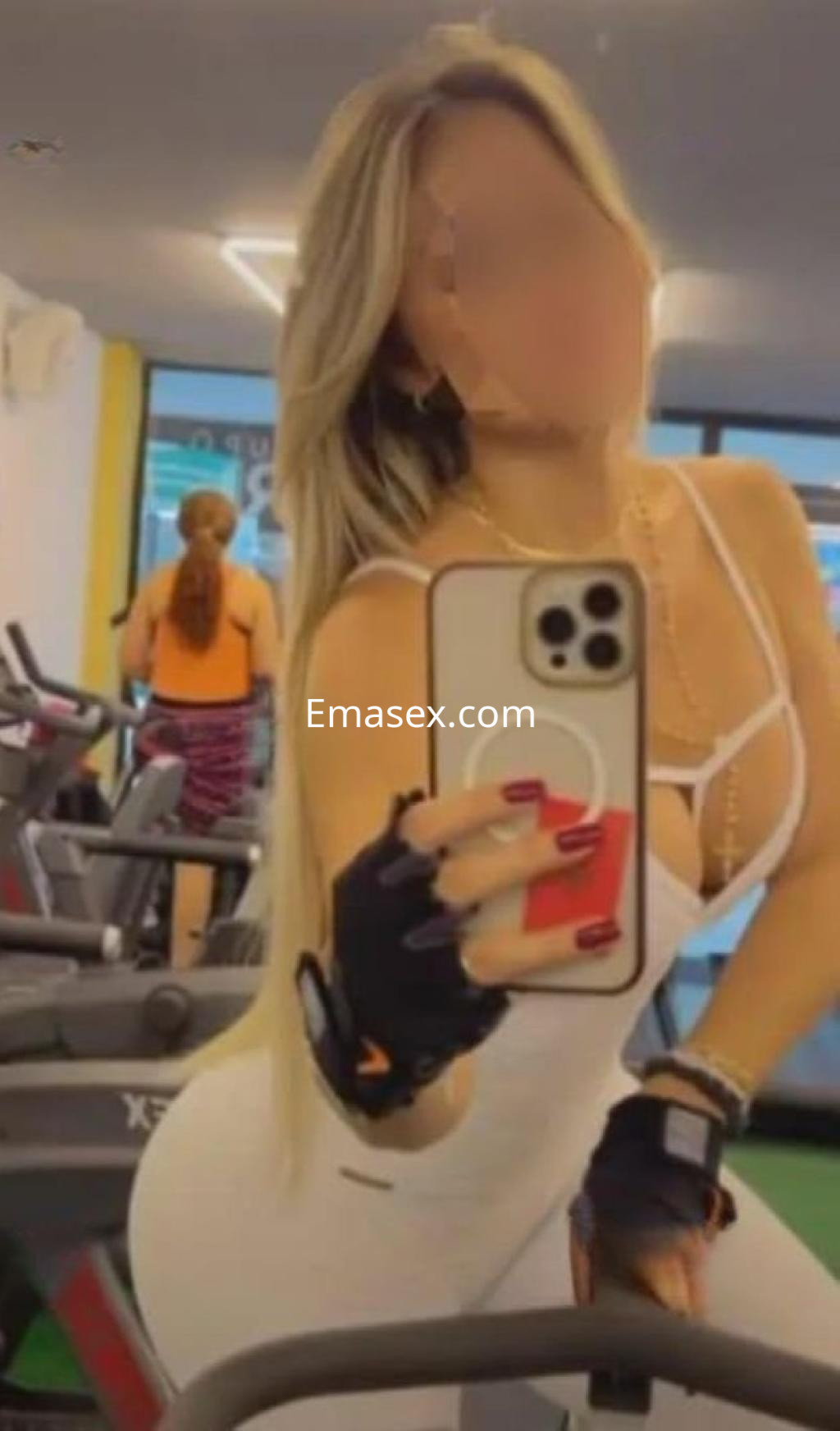 Puta en Sevilla, con cabello rubio largo, vestida en un conjunto deportivo blanco, posando en un gimnasio.