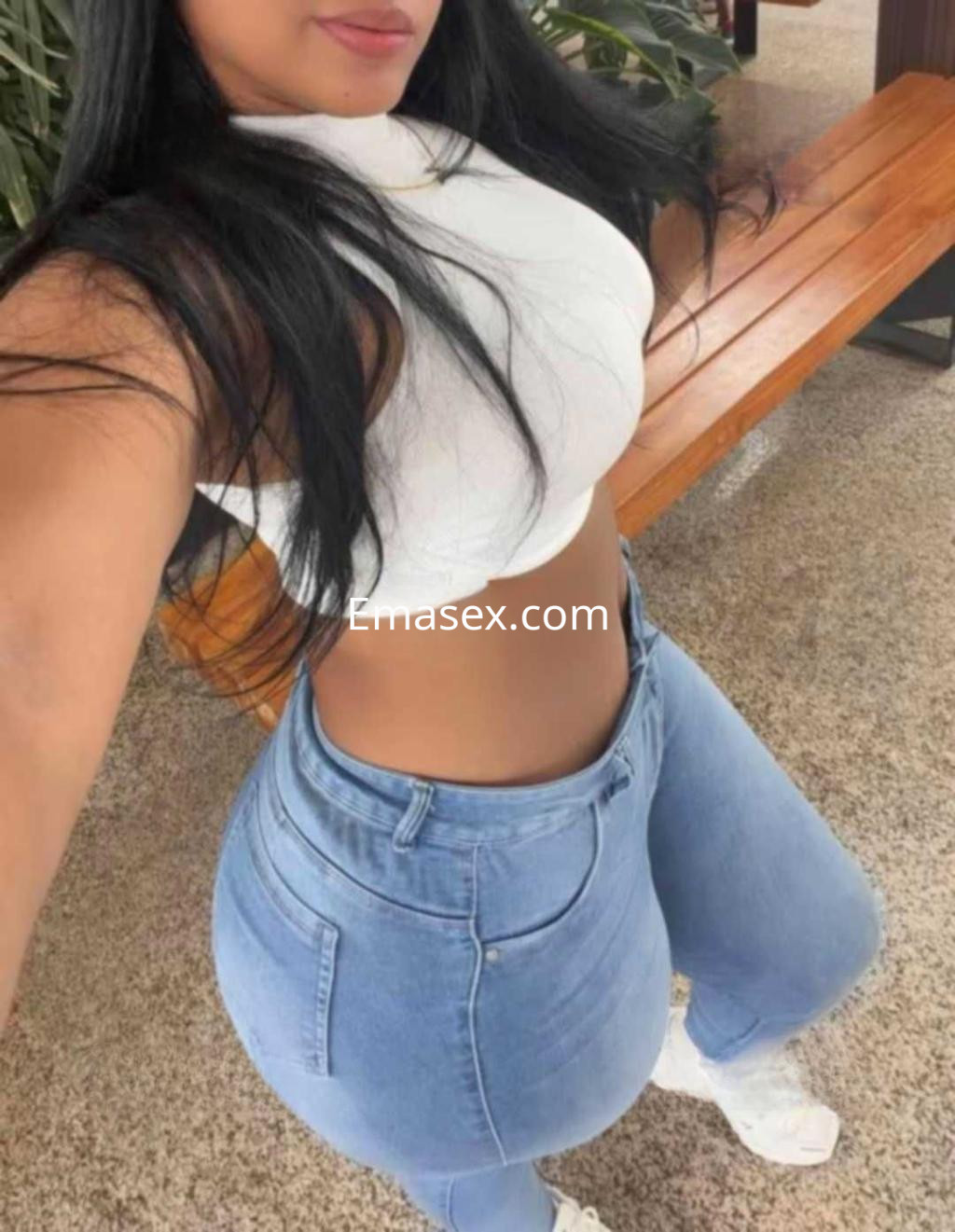 Escort en Toledo con top blanco ajustado y jeans claros, posando en un entorno al aire libre.