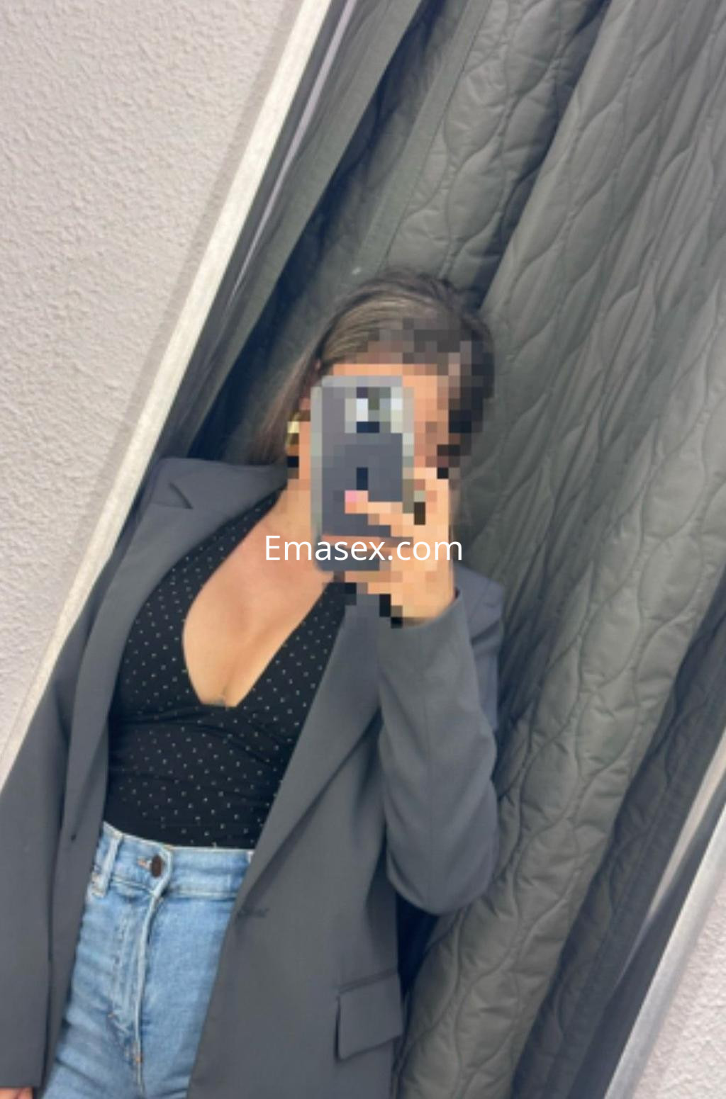 Escort en Valladolid con blazer gris y top negro de puntos, posando frente a un espejo.