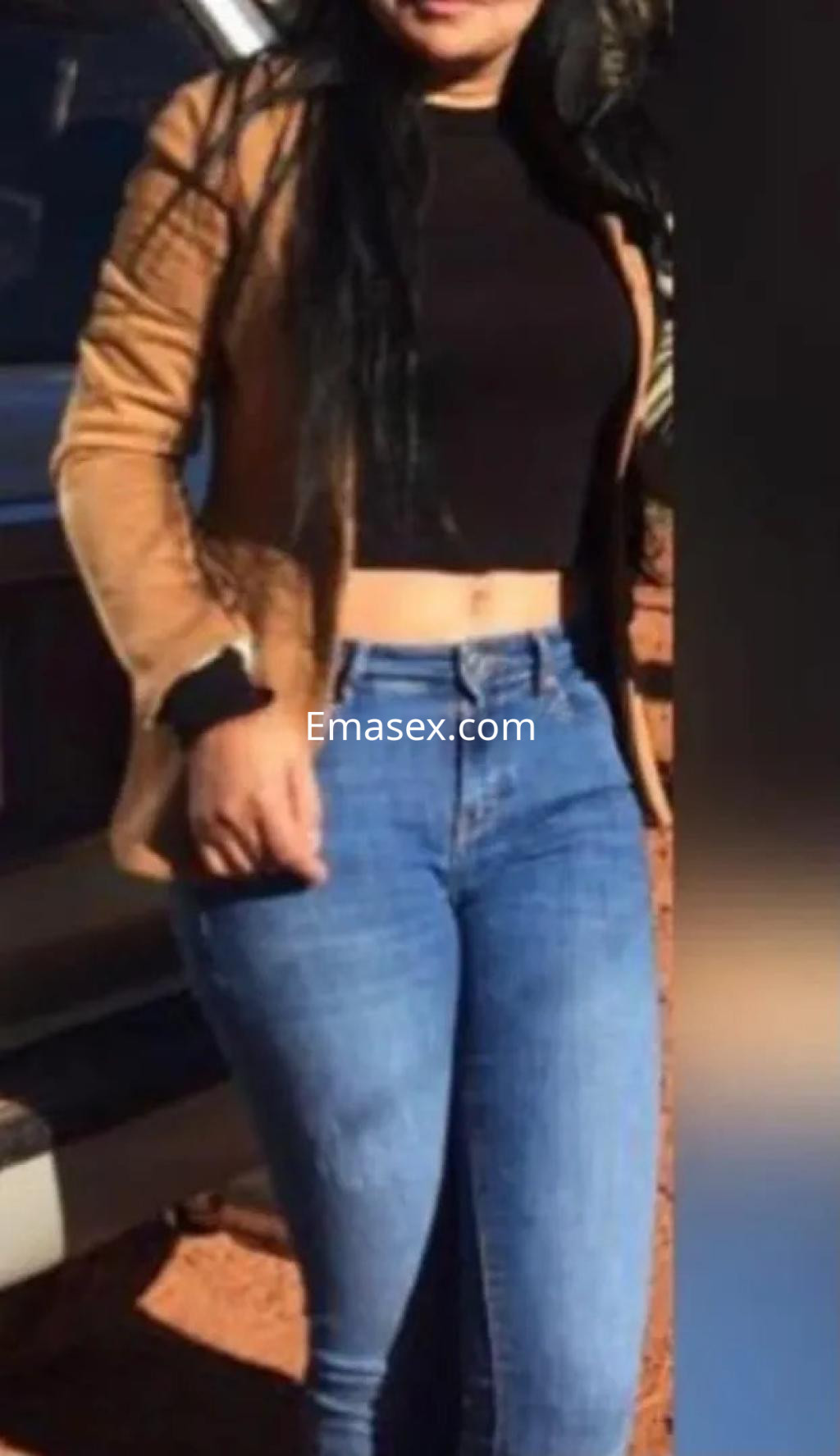Puta con chaqueta marrón y top negro, luciendo jeans ajustados en un entorno exterior en Valladolid.