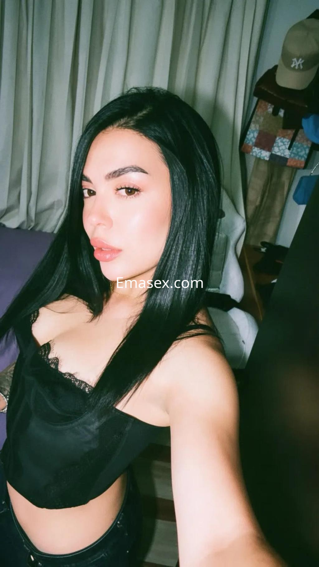 Escort en Alicante con cabello largo y lacio, luciendo un top negro sin mangas y posando en un ambiente interior.