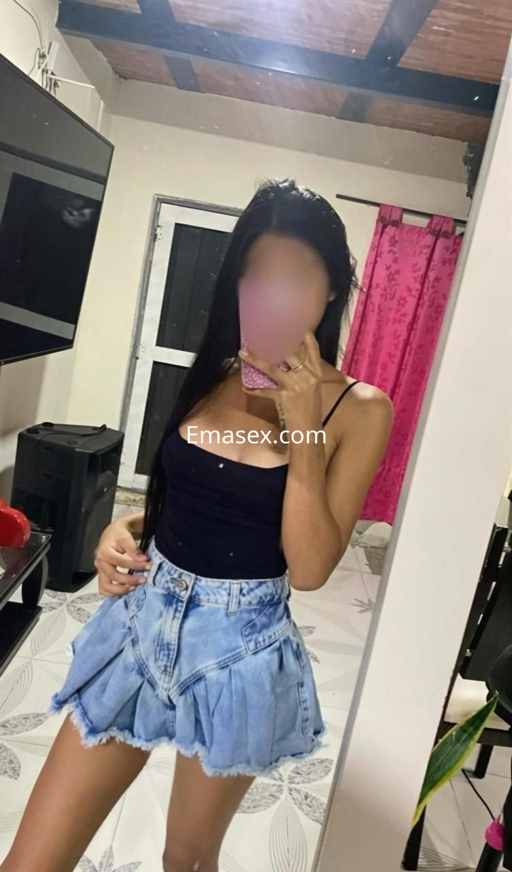 Puta en Madrid luciendo un top negro sin mangas y un short de mezclilla mientras se toma una selfie en el espejo.
