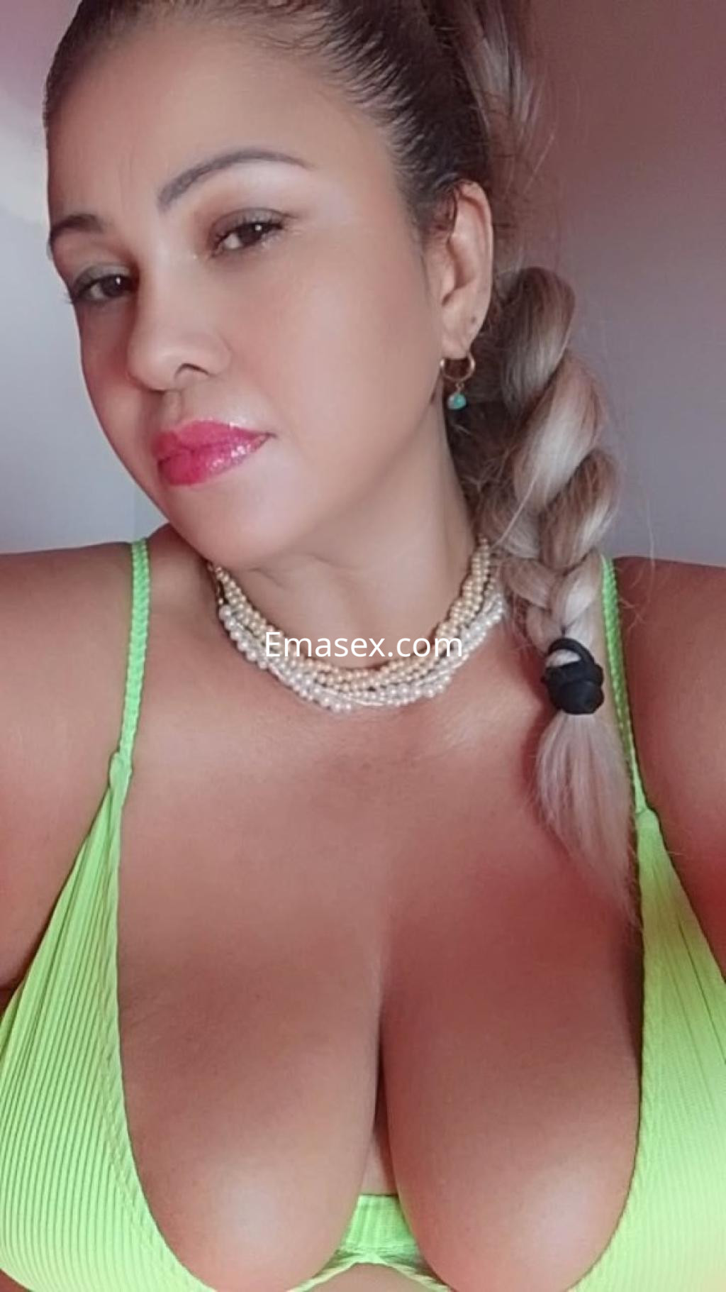 Escort en Santander luciendo un bikini verde, con cabello trenzado y joyas, posando de perfil.