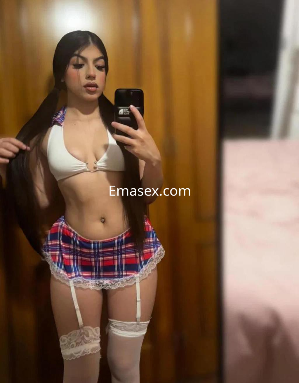 Escort en Tenerife posando con un top blanco y una minifalda de cuadros, mostrando un look juvenil y coqueto.