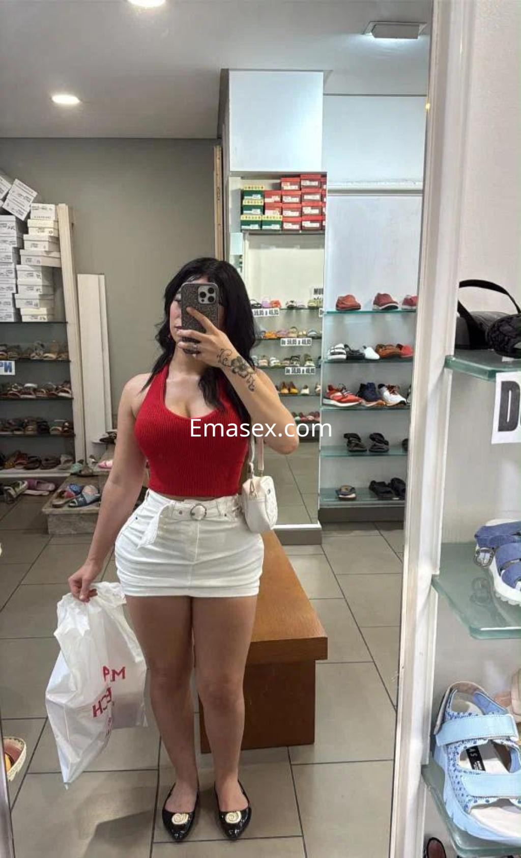 Escort en Toledo, con top rojo y pantalones cortos blancos, sosteniendo una bolsa en una tienda de calzado.
