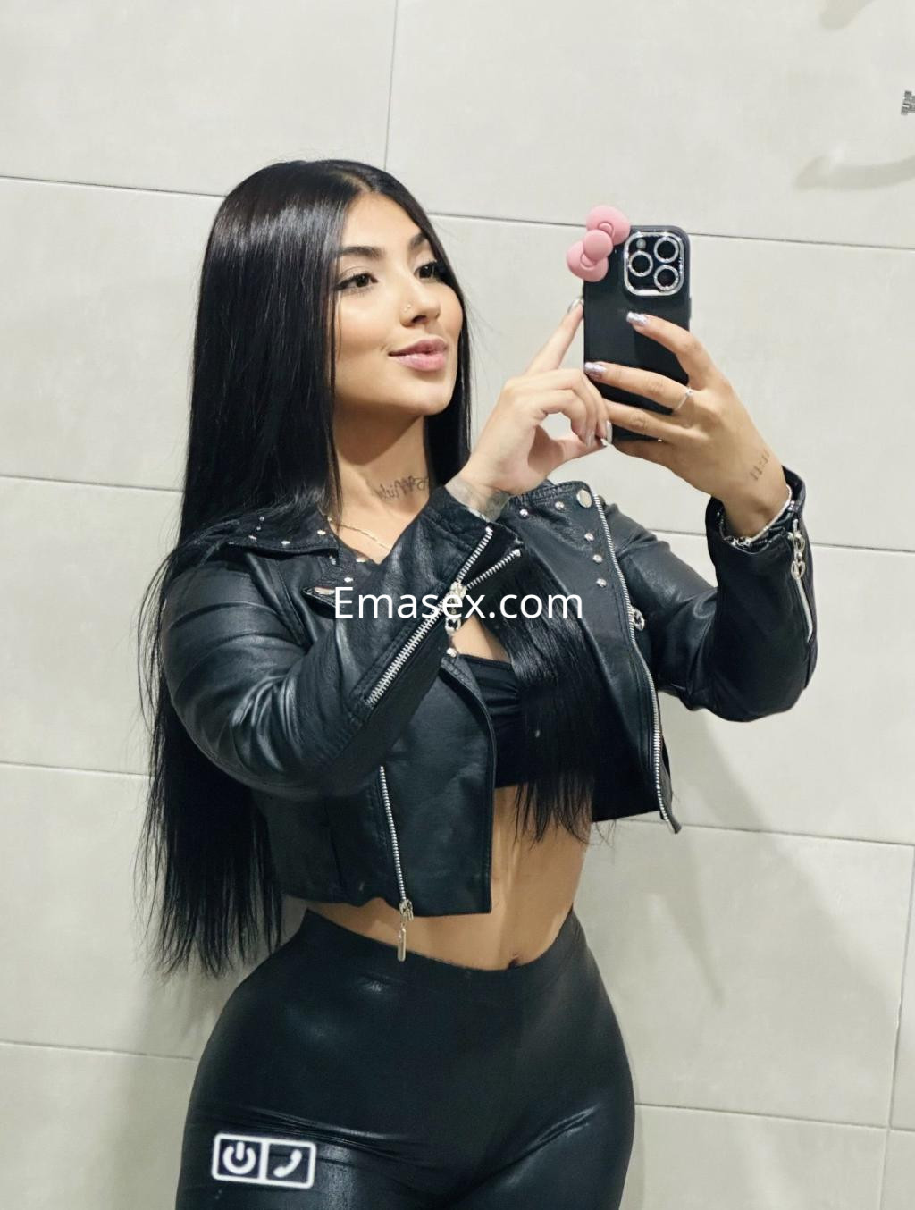 Escort en Cádiz, posando frente al espejo con chaqueta de cuero negra y leggins ajustados, mostrando su cabello largo y lacio.